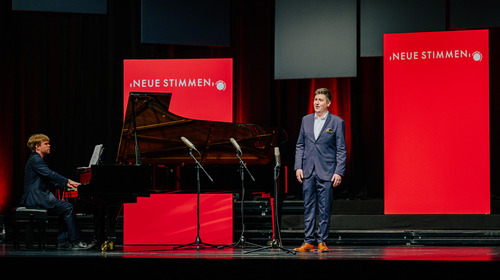 Kieran Carrel, participant of the NEUE STIMMEN 2022 competition, sings on stage during auditions at the final round in Gütersloh. Next to him, a pianist playing the piano can be seen.