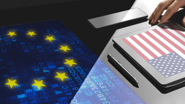 Geschäftsmann bei der Arbeit im Büro mit Bildschirmtechnik. Auf seinem Tablet ist eine Abbildung der amerikanischen Flagge und vor ihm auf dem Schreibtisch eine Abbildung der EU-Flagge.