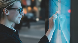 Junge Frau mit Brille vor einer digitalen Tafel.