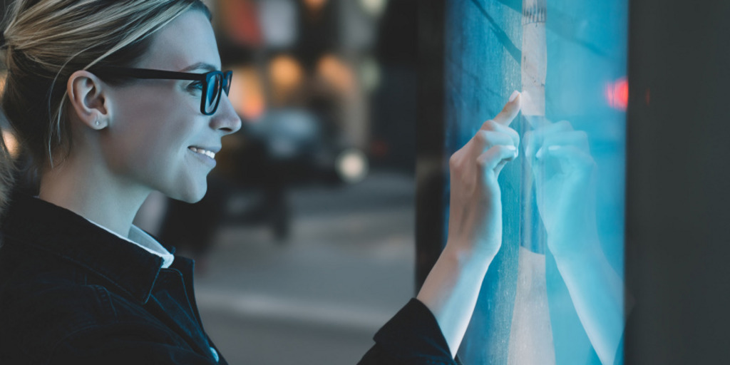 Junge Frau mit Brille vor einer digitalen Tafel.