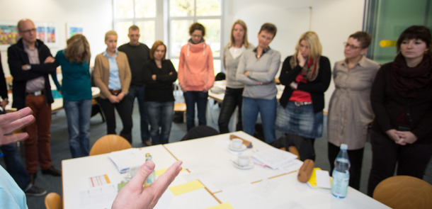 Lehrer und Lehrerinnen stehen in einem Klassenraum und hören dem Redner zu