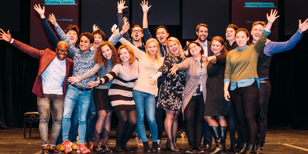 Group picture of the NEUE STIMMEN 2017 semifinalists. The singers stand on a stage and celebrate.