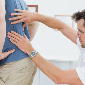 Ein Arzt tastet den Rücken eines Patienten ab.