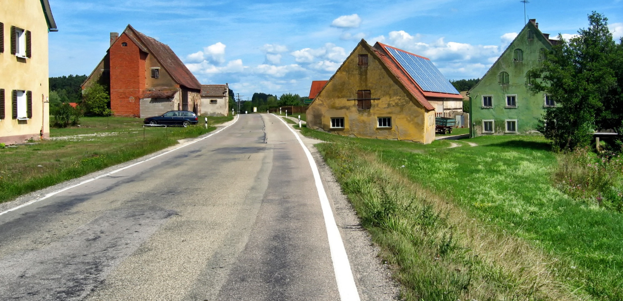 Eine verlassene Straße in einem bayrischen Dorf mit heruntergekommenen Häusern am Straßenrand.