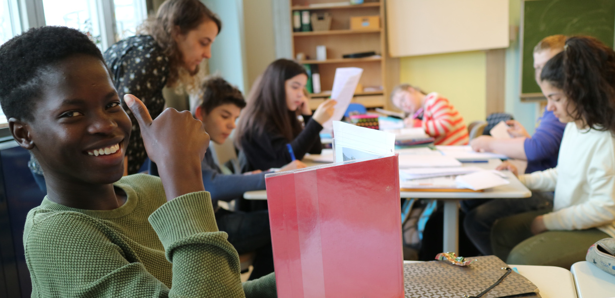 Aufnahme aus der AG "Inklusion an Oldenburger Schulen", einer der Preisträger des Jakob Muth-Preises 2017. Ein Schüler sitzt an einem Tisch in einem Klassenzimmer, lächelt in die Kamera und macht "den Daumen hoch". Vor ihm steht ein aufgeschlagenes Buch auf dem Tisch. Im Hintergrund sitzen fünf weitere Schüler an einem Tisch und lesen. Über den Tisch gebeut steht eine Lehrerin.