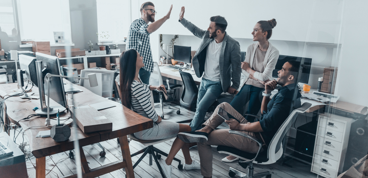 Eingekauft am 04.04.2018 für ST-BS; Meldung „Mein gutes Beispiel“; Büroalltag; High-five for success! Two cheerful young business people giving high-five while their colleagues looking at them and smiling