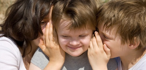 Zwei Schüler flüstern einem dritten etwas in die Ohren.
