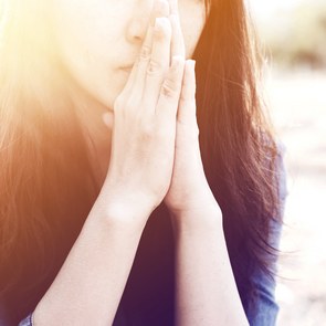 Woman praying in meadow at sunset