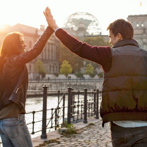 [Translate to English:] Zwei junge Menschen klatschen in die Hände ein während in an der Spree in Berlin stehen.