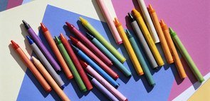 Wachsmalstifte liegen auf buntem Tonpapier.