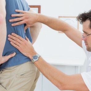 Ein Arzt tastet den Rücken eines Patienten ab.