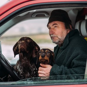 Heiner Sindel blickt aus dem geöffneten Fenster seines Autos. Er hat zwei Hunde auf seinem Schoß sitzen.