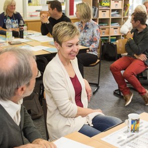 Lehrer sitzen in Gruppen an Schreibtischen und diskutieren