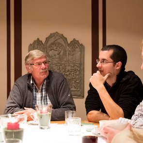 Mehrere Menschen sitzen um einen Tisch herum und besprechen diverse Themen.