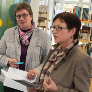 Zwei Frauen stehen vor einer Glaswand und sprechen miteinander