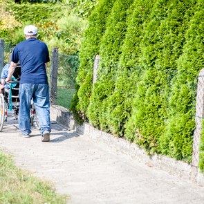 Mann geht mit Frau im Rollstuhl spazieren