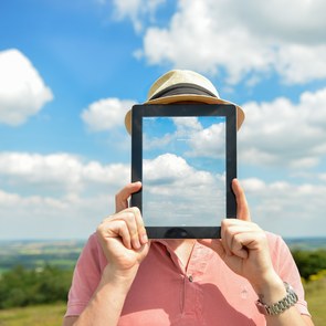 Tablet verdeckt Gesicht eines Mannes auf einer Wiese
