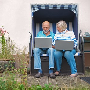 Seniorenpaar sitzt in Strandkorb und schaut auf Laptops